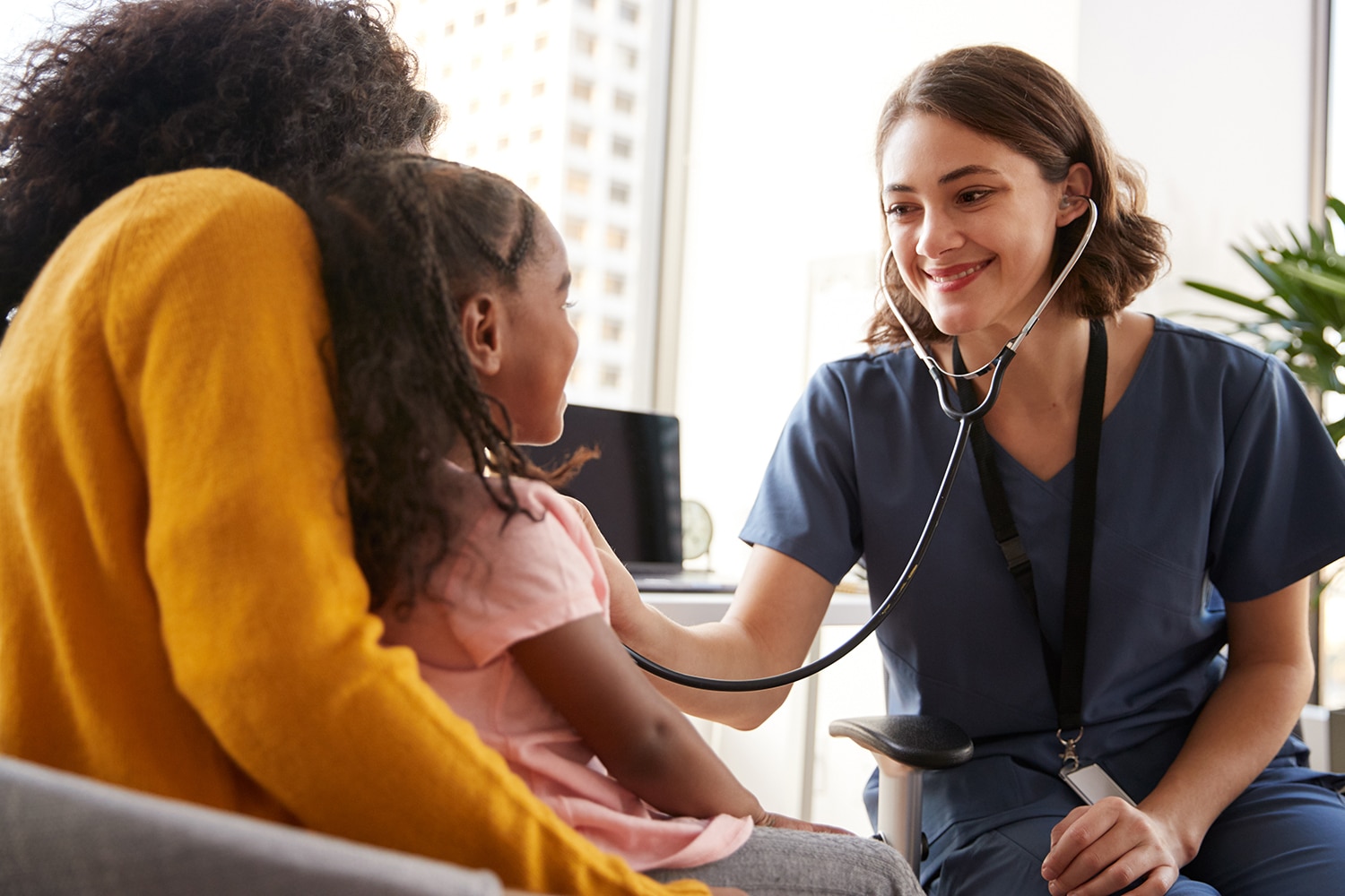 smiling pediatrician holding stethoscope to patient's chest.